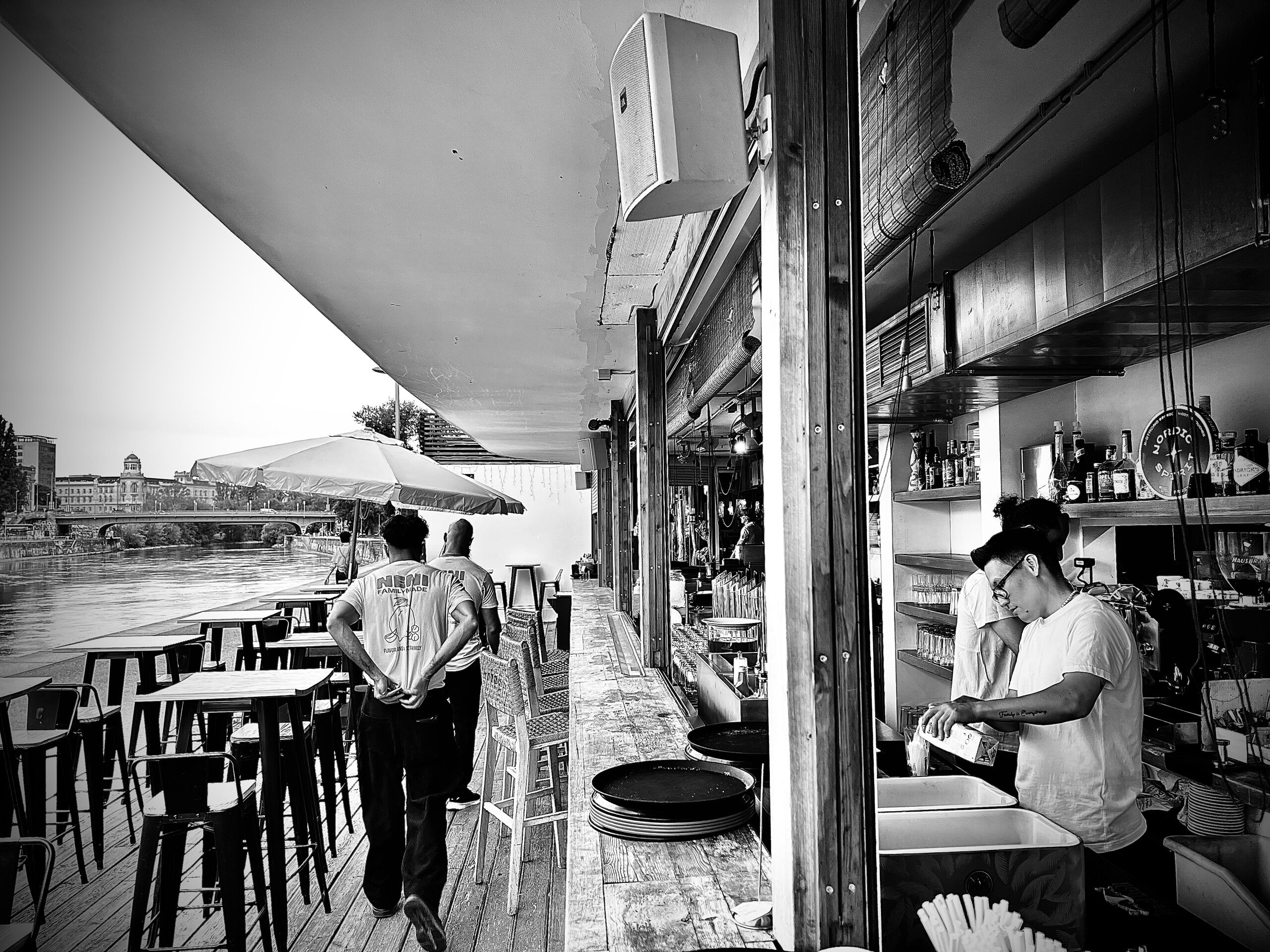 A bar on the Danube canal: stools on a wooden deck, the counter behind, water and a bridge to the left.