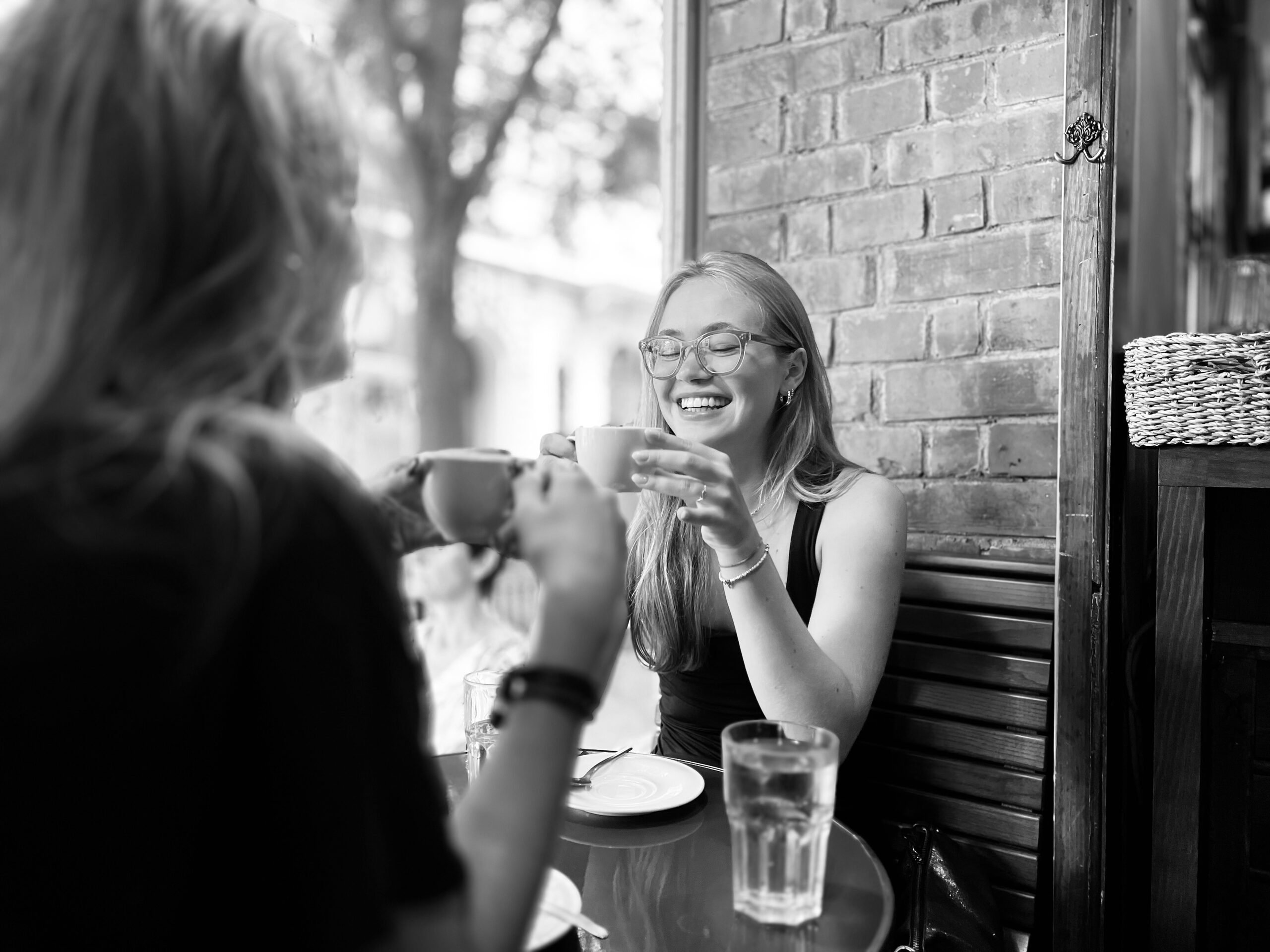 Two women at an outdoor café table, one holding her cup in both hands.