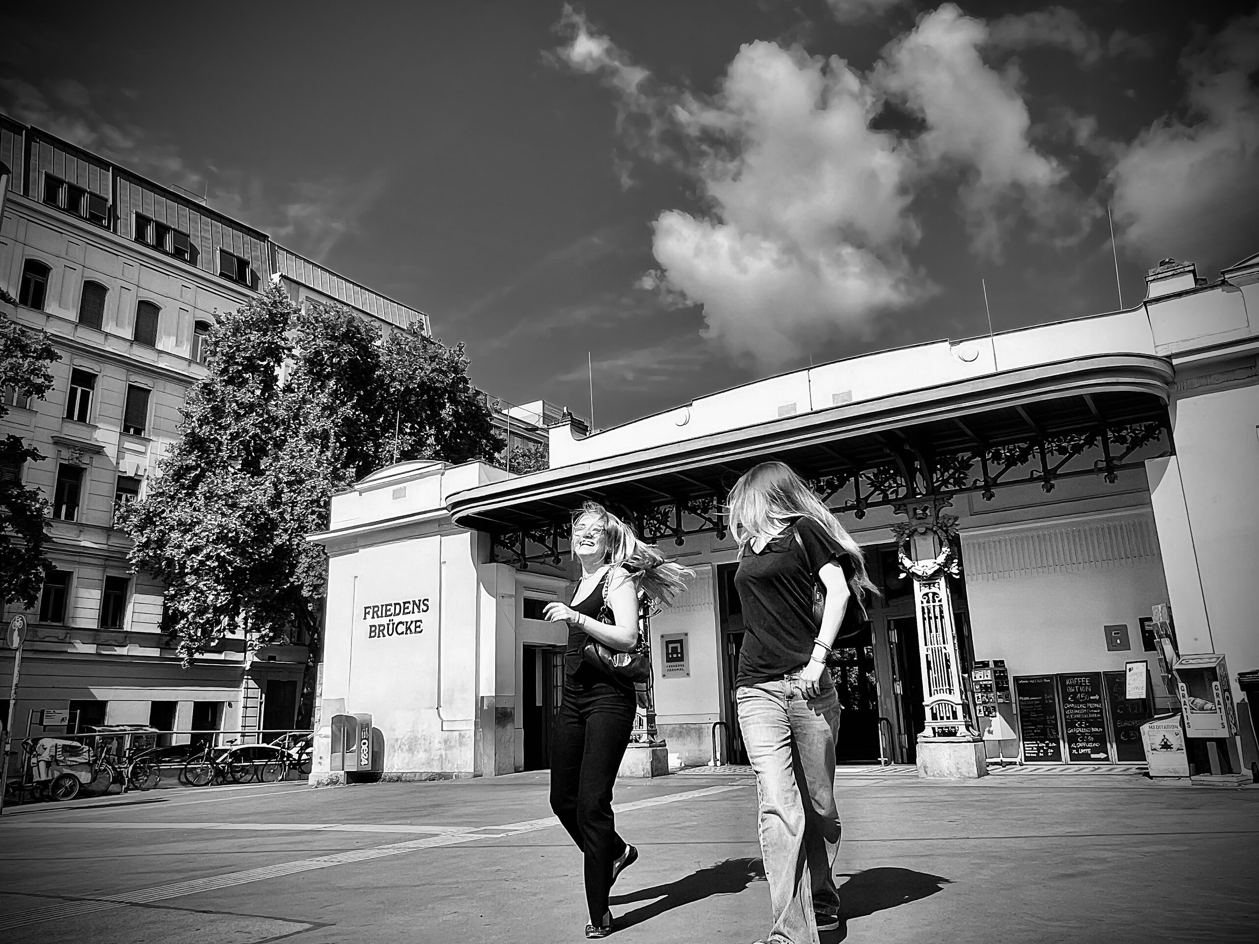 At the Friedensbrücke station building: two women in front of it under a clouded sky.
