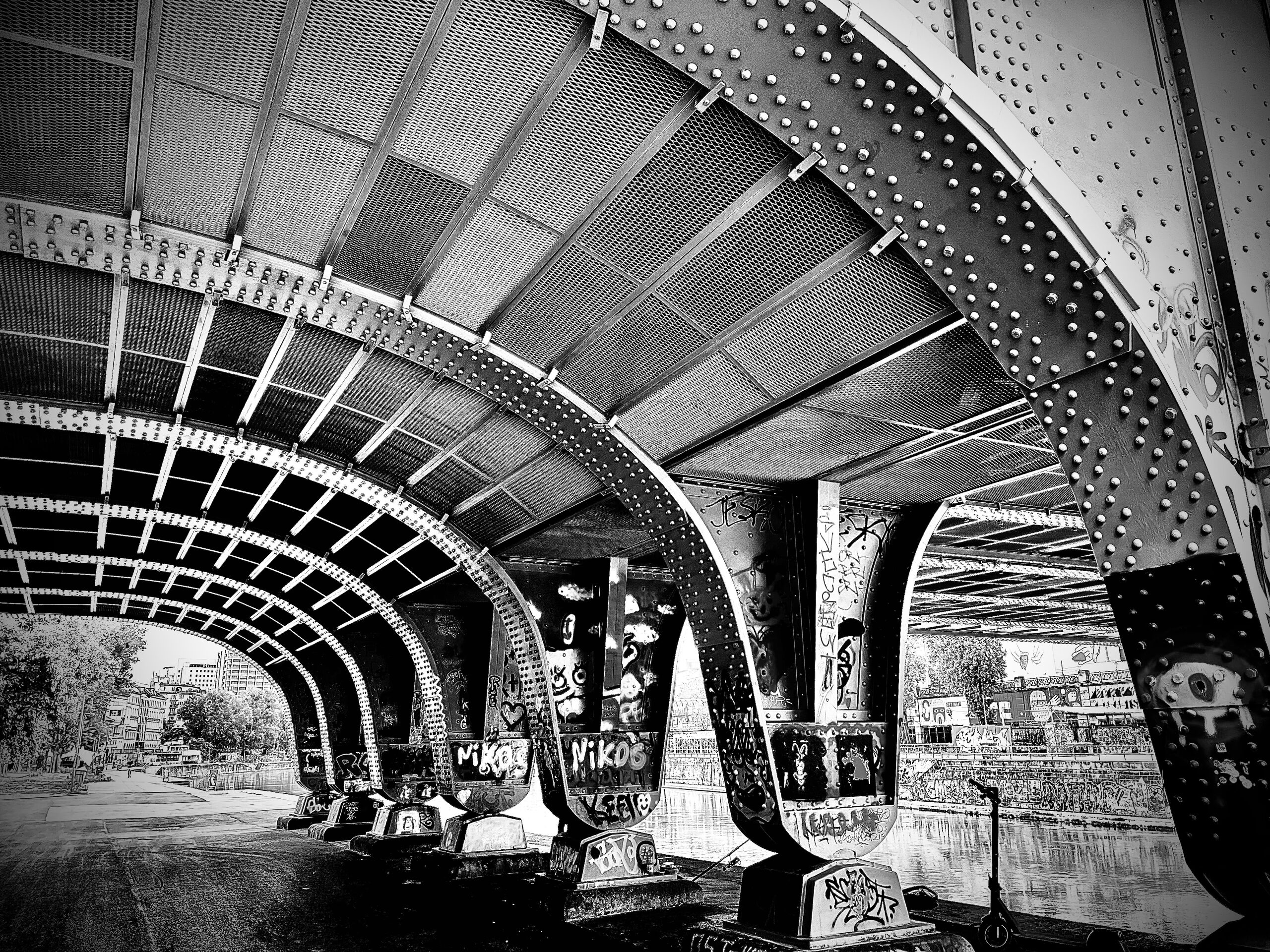 Under the bridge: riveted steel arches, graffitied piers and the path along the canal.
