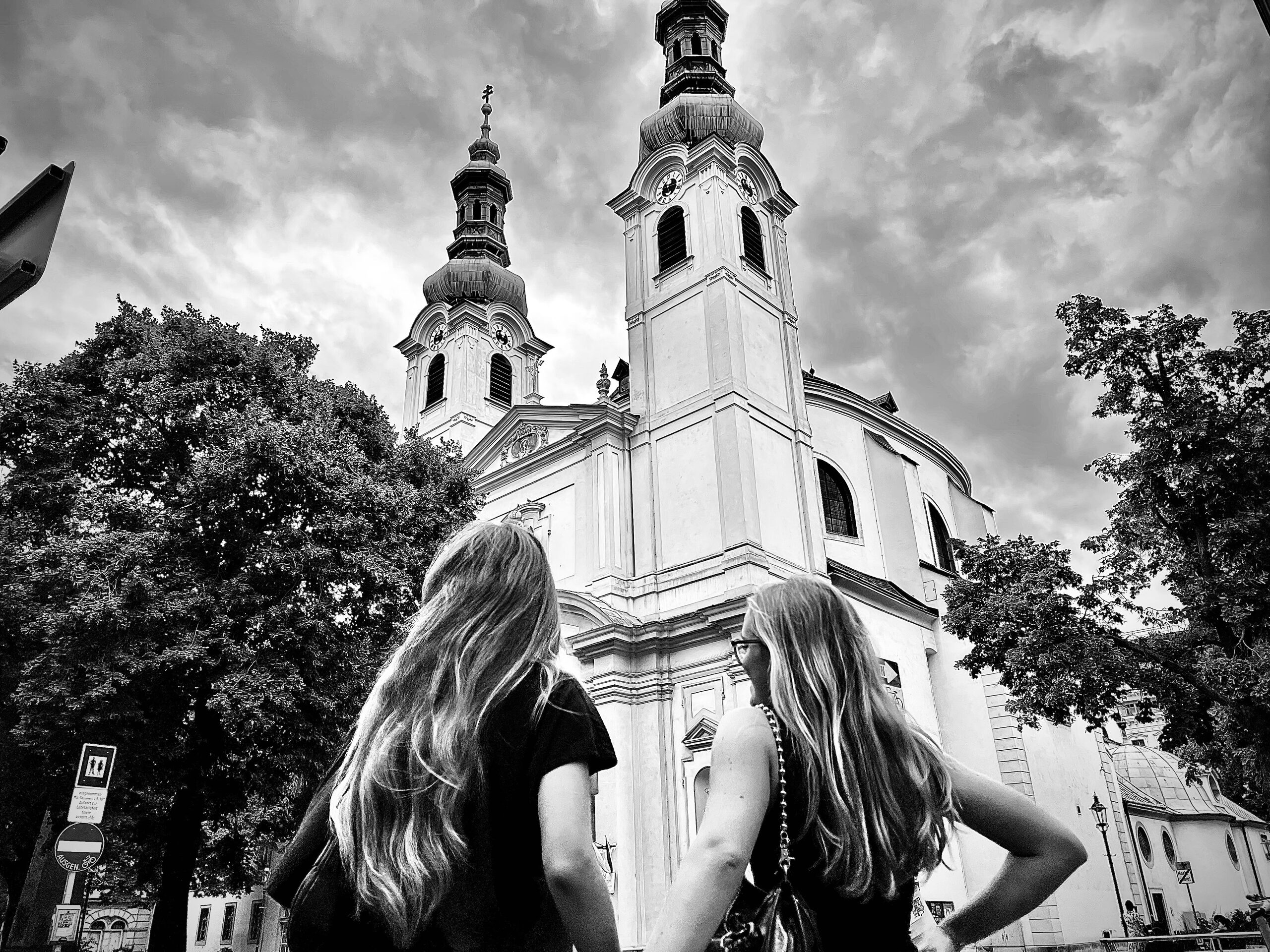 A baroque church with two towers, two women below among the trees.