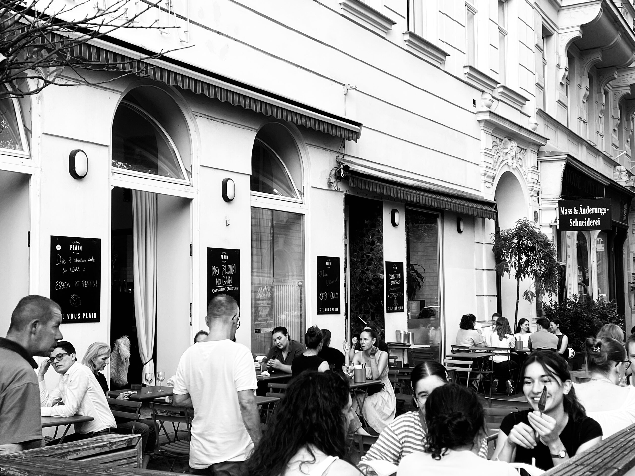 The entrance of a bar beneath round arches, guests at outdoor tables in front.